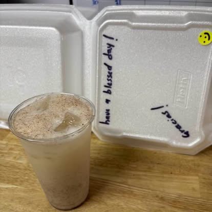 A cup of horchata dusted with cinnamon next to a to-go box that reads have a blessed day and gracias