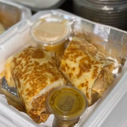 A toasted wrap cut in half, filled with meat, with two cups of sauce
